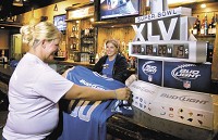 Server Brooke Stout and bartender Ashley Johnson, who work at Montana Mike's Steak House, examine material the business has received to help promote Super Bowl activities in the area. John P. Cleary photo