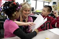 Jeanine Reynolds, a second-grade teacher&nbsp;at Emmons Elementary, smiles as she looks over work from Nykeria Harper, left, and Riley Penrod during a free-write session on Wednesday, Feb. 29, 2012, in Mishawaka. (South Bend Tribune/JAMES BROSHER) 