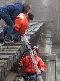 South Bend firefighters Steve Pritz, right, and Dave Pritz, center, work Friday with University of Notre Dame student Angelene Dascanio as they take measurements to assess the structural integrity of the abandoned railroad bridge near Angela Boulevard and Riverside Drive. SBT Photo/ROBERT FRANKLIN
