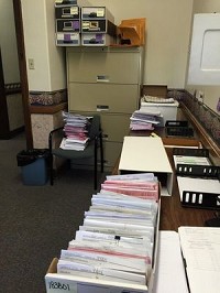 Bill invoices, some dating to late March, are stacked on a chair, below boxes where past invoices are stored in the city&rsquo;s controller office. The boxes are audited annually by the state. Staff photo by Howard Greninger