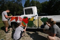 Noblesville High School art teacher, Kayti Hahn paints the new farmer&rsquo;s market truck with two students.