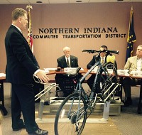Northern Indiana Commuter Transportation District General Manager Michael Noland shows board members a rack that can be used to carry bicycles on South Shore trains at a meeting in July. Staff photo by Deborah Laverty