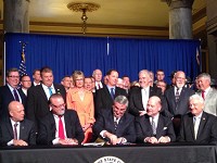 Hoosier lawmakers were all smiles as Republican Gov. Eric Holcomb, seated center, signs their road funding plan into law Thursday. Staff photo by Dan Carden