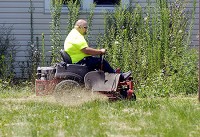 Jimmy Vest cuts a path through tall grass as he mows this lot in Elwood on Tuesday. Vest, a part-time landscaper, was hired by the city to mow neglected properties. Staff photo by John P. Cleary