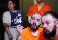 Nicholas Karagianis holds up a book entitled, I am a Heroin Addict, during a weekly meeting with people struggling with addiction. Staff photo by Tom Russo