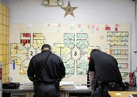Officers work in the book-in area&nbsp;of the Madison County Jail. Each piece of paper on the board represents an inmate housed at the jail. The county jail was built to house 207 inmates but had 305 on Wednesday. Staff photo by Don Knight