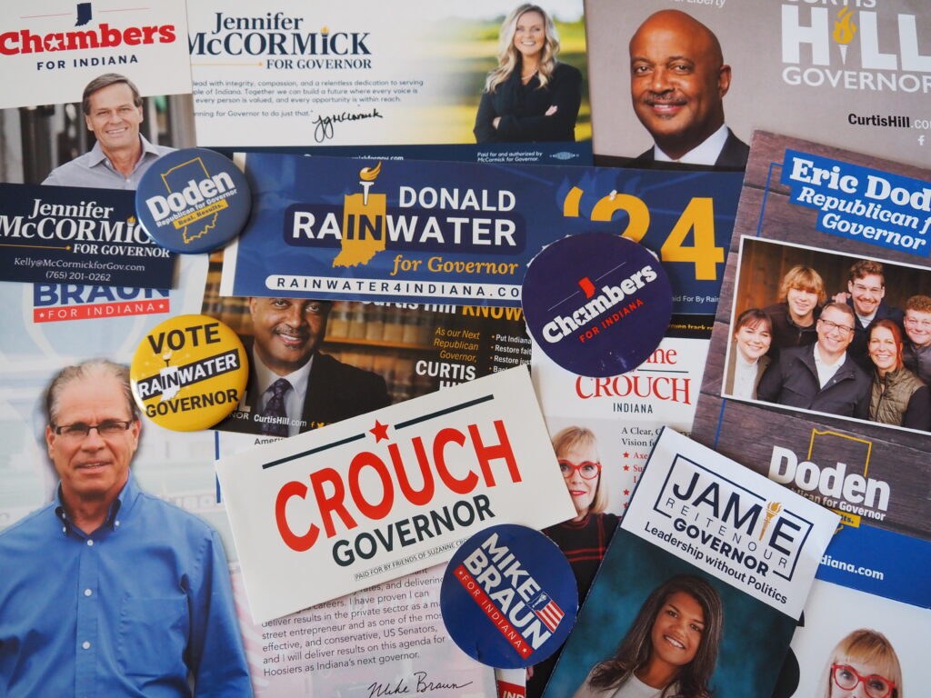 Campaign materials from the eight gubernatorial candidates who appeared at a business-friendly forum on taxes and government on March 19, 2024. (Whitney Downard/Indiana Capital Chronicle)
